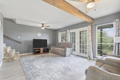 Living area with a ceiling fan, french doors, a textured ceiling, beam ceiling, and light wood-style floors