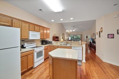 Kitchen with white appliances, vaulted ceiling, a peninsula, light wood-style flooring, and light countertops