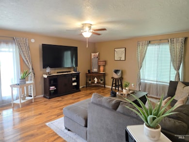 Living area featuring ceiling fan, plenty of natural light, wood finished floors, and a textured ceiling