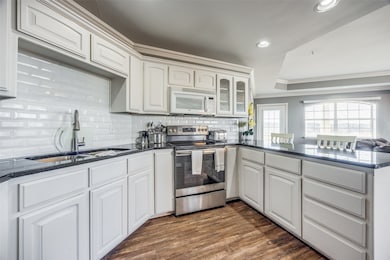 Kitchen featuring backsplash, stainless steel electric range, kitchen peninsula, sink, and white cabinetry