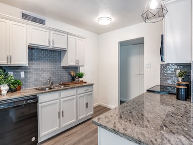 Kitchen featuring backsplash, black dishwasher, light stone counters, light wood-style flooring, and white cabinets