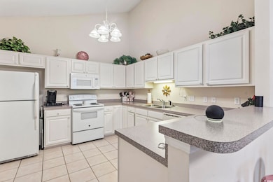 Kitchen with pendant lighting, white appliances, white cabinetry, a peninsula, and light tile patterned floors