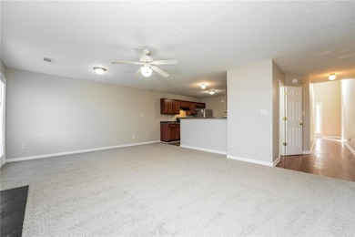 Unfurnished living room featuring light carpet, ceiling fan, and a textured ceiling