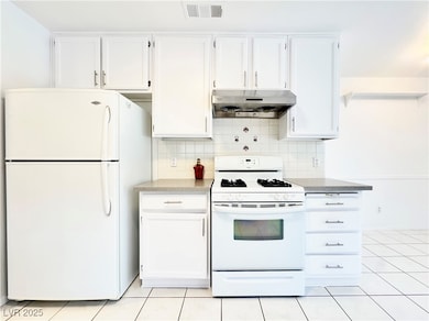 Kitchen featuring white appliances, white cabinets, decorative backsplash, light tile patterned floors, and under cabinet range hood