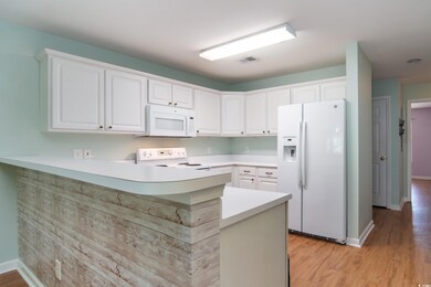 Kitchen featuring white appliances, a peninsula, white cabinetry, light countertops, and light wood-type flooring