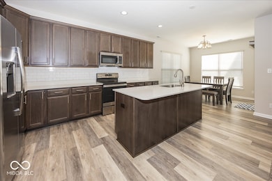 kitchen featuring wood cabinetry, tasteful backsplash, stainless steel appliances,solid surface counter and  a center island with sink, and decorative light fixtures