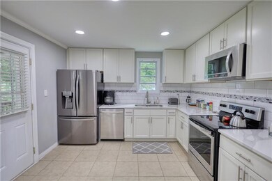 Kitchen featuring stainless steel appliances, a sink, tasteful backsplash, light countertops, and white cabinets