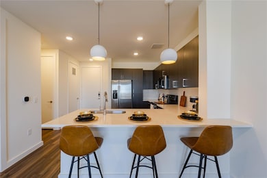 Kitchen with stainless steel appliances, light countertops, a breakfast bar, a sink, and dark wood-type flooring
