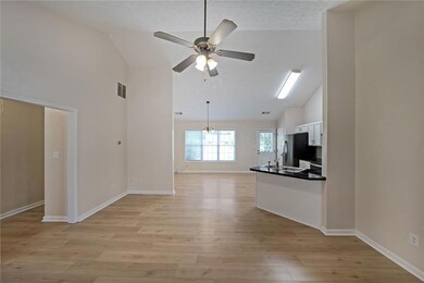 Unfurnished living room featuring ceiling fan, a chandelier, light wood-style flooring, high vaulted ceiling, and a textured ceiling