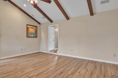 Empty room with light wood-style flooring, vaulted ceiling with beams, baseboards, visible vents, and a ceiling fan