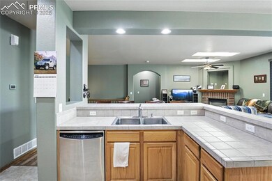 Kitchen featuring stainless steel dishwasher, tile counters, open floor plan, a skylight, and a fireplace