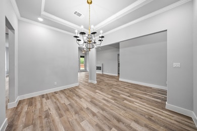 Unfurnished dining area featuring a raised ceiling, ornamental molding, light wood-style flooring, a chandelier, and recessed lighting