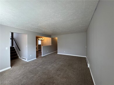 Carpeted spare room with a textured ceiling, a notable chandelier, and a baseboard heating unit