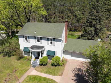 View of front facade featuring a chimney, a garage, driveway, roof with shingles, and a view of trees