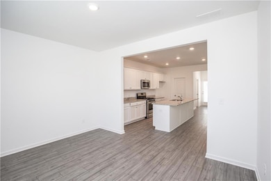 Kitchen with stainless steel appliances, recessed lighting, light wood-type flooring, white cabinetry, and a center island with sink