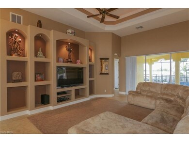 The impressive and inviting living room features tile floors, lit tray ceiling with designer fans trimmed in crown molding, custom made recess lit built in and sliding doors leading to the lanai.