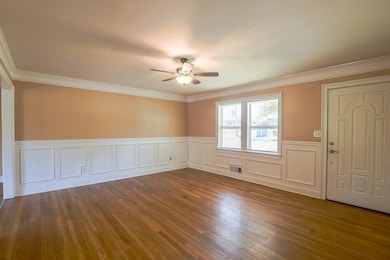Unfurnished room featuring wood finished floors, a wainscoted wall, a decorative wall, ornamental molding, and a ceiling fan