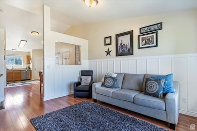Living area featuring vaulted ceiling, wood finished floors, a decorative wall, and a wainscoted wall