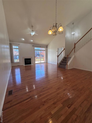 Unfurnished living room featuring stairway, a chandelier, dark wood-style flooring, ceiling fan, and high vaulted ceiling