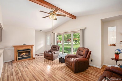 Living area with a glass covered fireplace, light wood finished floors, and ceiling fan