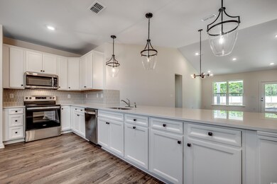 Kitchen with appliances with stainless steel finishes, a sink, light countertops, white cabinets, and vaulted ceiling