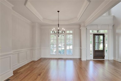 Foyer entrance featuring a tray ceiling, a chandelier, light wood finished floors, a decorative wall, and wainscoting