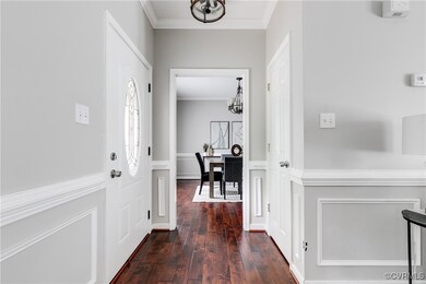 Bright and welcoming foyer with elegant wainscoting, rich hardwood floors, and a clear view into the formal dining room