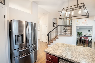 Kitchen featuring stainless steel fridge, light wood finished floors, granite countertops, pendant lighting, vaulted ceiling, stylish handrail