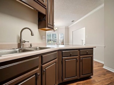 Kitchen featuring ornamental molding, a textured ceiling, dark wood finished floors, a peninsula, and light countertops