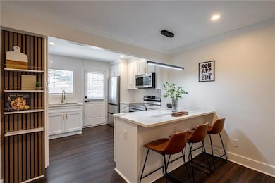 Kitchen with stainless steel appliances, a peninsula, white cabinetry, dark wood-style flooring, and crown molding