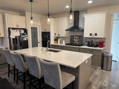 Kitchen featuring decorative backsplash, wall chimney exhaust hood, black appliances, a breakfast bar area, and recessed lighting