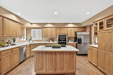 Spacious kitchen with an abundance of oak cabinetry, a large center island with cooktop, double wall ovens, and stainless-steel appliances. Bright recessed lighting and hardwood floors create a warm and functional space.