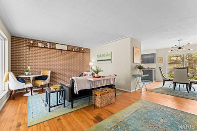 Dining room with brick wall, wood finished floors, a chandelier, and an accent wall
