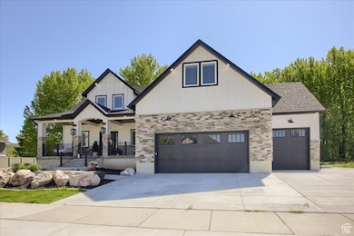 View of front of property featuring a porch, driveway, stone siding, a garage, and roof with shingles
