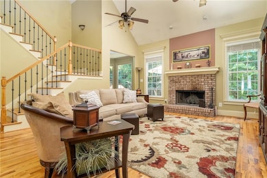 Living room with a ceiling fan, wood finished floors, plenty of natural light, stairs, and high vaulted ceiling