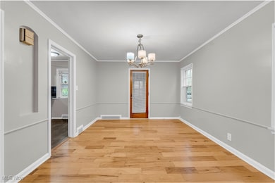 Unfurnished dining area featuring crown molding, a chandelier, and light wood-style floors