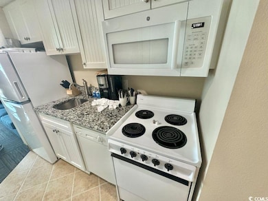 Kitchen featuring white appliances, light stone counters, white cabinets, and light tile patterned floors