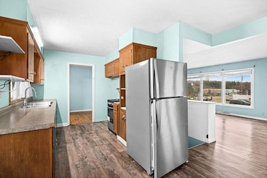 Kitchen with appliances with stainless steel finishes, brown cabinets, dark wood-type flooring, open shelves, and a textured ceiling