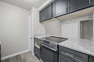Kitchen with stainless steel electric range oven, light stone counters, light wood-style flooring, gray cabinetry, and a textured ceiling