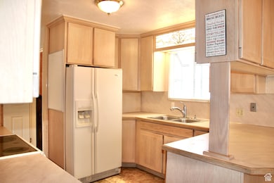 Kitchen featuring white fridge with ice dispenser, light countertops, and light brown cabinets