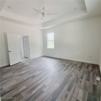 Empty room featuring a tray ceiling, wood finished floors, and baseboards