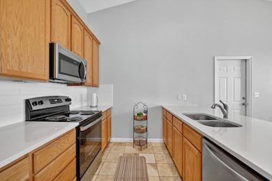 Kitchen featuring appliances with stainless steel finishes, light stone counters, tasteful backsplash, light tile patterned flooring, and a peninsula