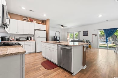 Kitchen with stainless steel appliances, ceiling fan, light wood-type flooring, a kitchen island with sink, and white cabinets