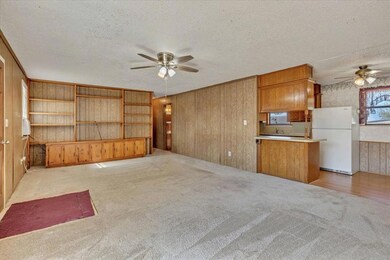 Unfurnished living room featuring a ceiling fan, light colored carpet, wood walls, and a textured ceiling