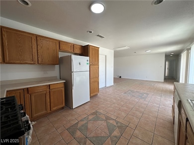 Kitchen with range with gas stovetop, brown cabinetry, freestanding refrigerator, light countertops, and recessed lighting