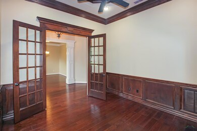 Unfurnished room with ornamental molding, a ceiling fan, dark wood-style floors, decorative columns, and wainscoting