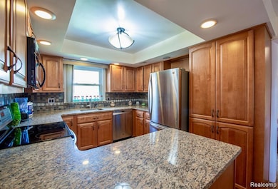 Kitchen featuring brown cabinetry, a tray ceiling, stainless steel appliances, light stone countertops, and tasteful backsplash
