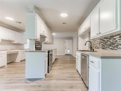 Kitchen with appliances with stainless steel finishes, a sink, backsplash, light wood-style floors, and crown molding