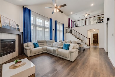 Living area with arched walkways, a tile fireplace, stairway, high vaulted ceiling, and wood finished floors