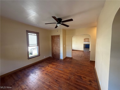 Unfurnished room with arched walkways, dark wood-style floors, and ceiling fan